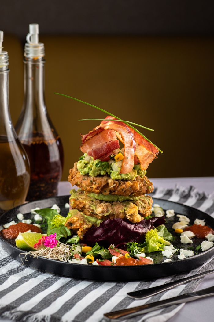 services-01 Enticing gourmet pancake stack with bacon, avocado, and vibrant salad on a black plate.